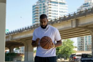 A man holding a basketball under a city bridge, conveying focus and urban sports atmosphere.