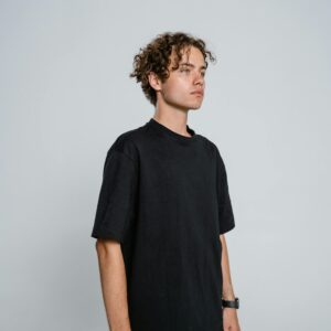 Teenage boy with curly hair posing in black t-shirt and tan pants indoors.
